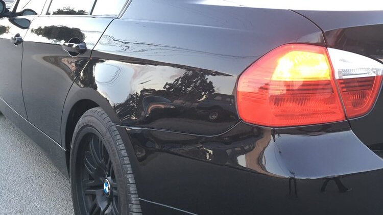 The rear quarter panel of a black sedan, smooth and glossy after the collision repair