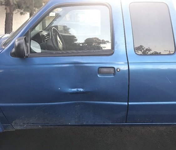 A blue pickup with a crease dent low on the driver door