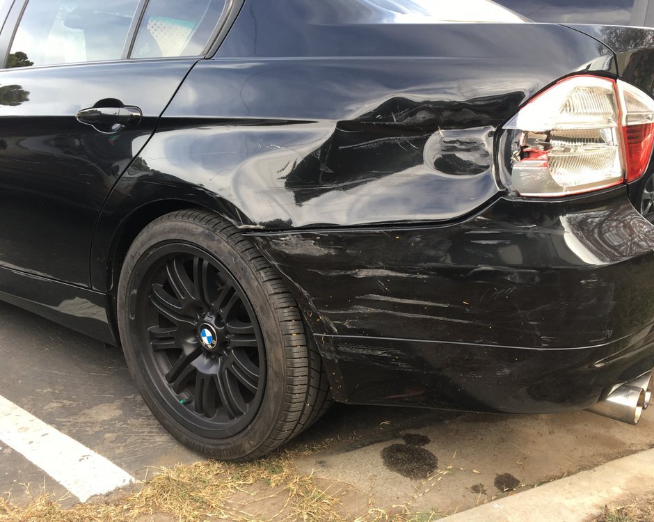 A black sedan with a crushed rear quarter panel and a torn bumper cover