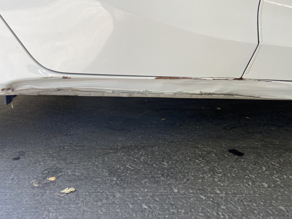 A white car with a crushed, rusting rocker panel under the doors